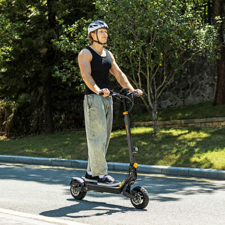 Person riding an electric scooter on a road with greenery in the background Ausom L1 Back To modern