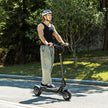 Person riding an electric scooter on a road with greenery in the background Ausom L1 Back To modern