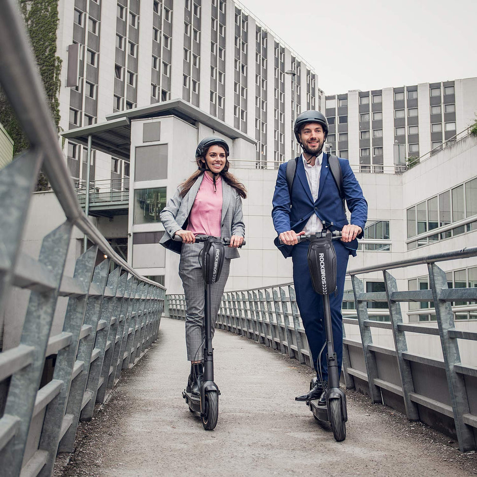 Two commuters riding electric scooters with ROCKBROS hard shell bags mounted on the stems